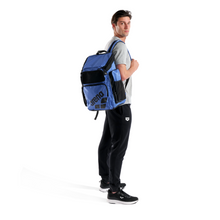 Load image into Gallery viewer, Person wearing a blue backpack with front arena branding on a white background