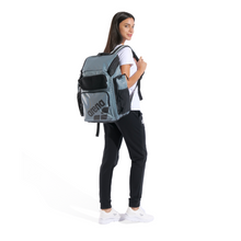 Load image into Gallery viewer, Woman wearing a sage green backpack with 'arena' branding on a white background